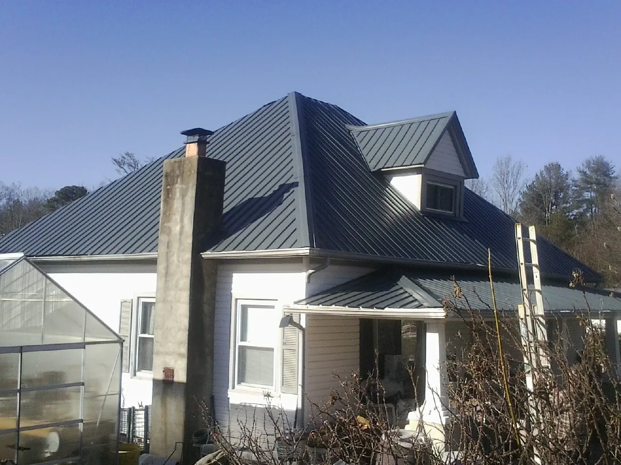 Dark blue standing seam metal roof on a white farmhouse with dormer — Slate & Tile Roof Repair by Roofing Brothers in Basom