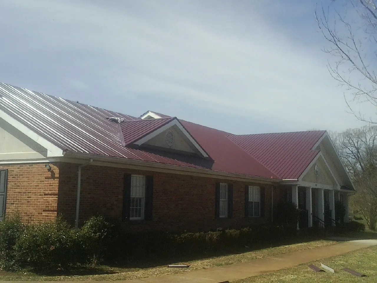 Red metal roof with gabled entries on a long brick building, from a Hail Damage Roof Repair job in Basom