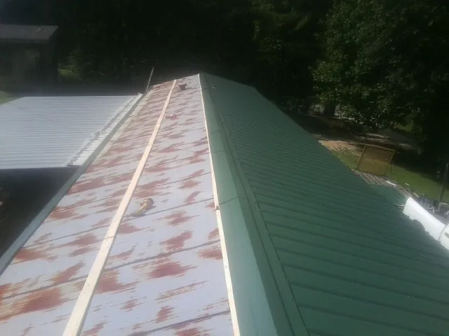 Old rusted panels beside newly installed green metal roofing — Wind Damage Roof Repair by Roofing Brothers in Basom