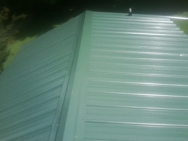 New green metal panels meeting at the ridge of a roof — Flat Roof Repair work by our crew in Basom