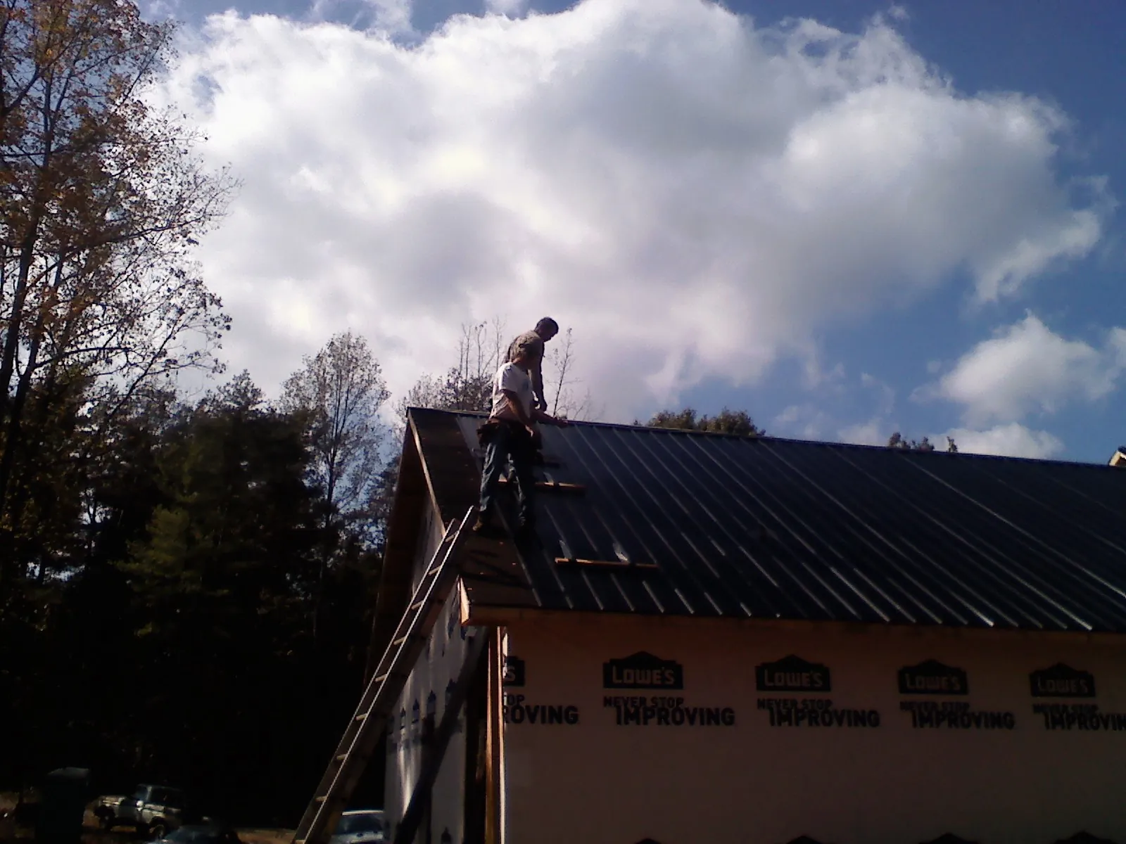 Roofer fastening dark metal panels high against a cloudy sky, from a Roof Inspection job in Basom